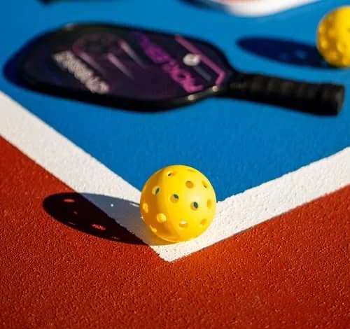 Perforated pickleball on the baseline of a blue and red court