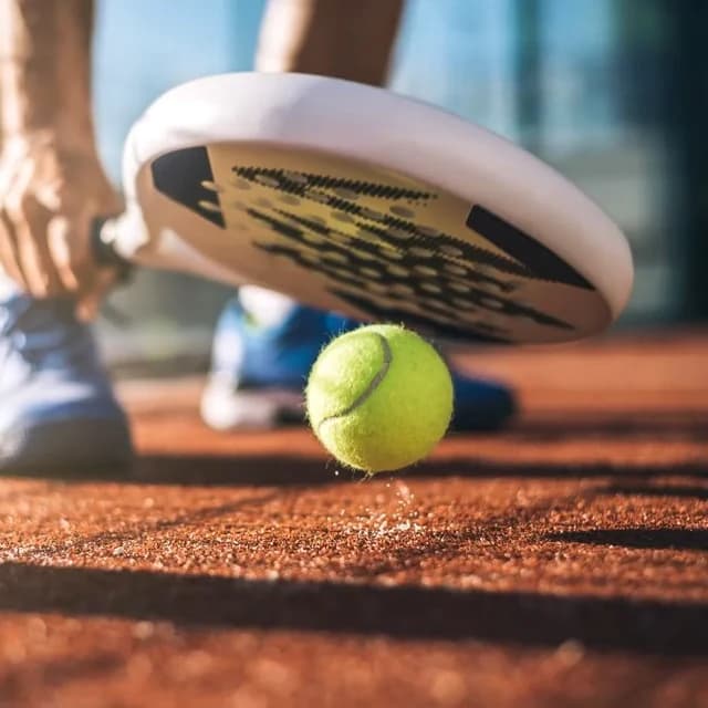 Padel racket and ball on a sunlit clay court
