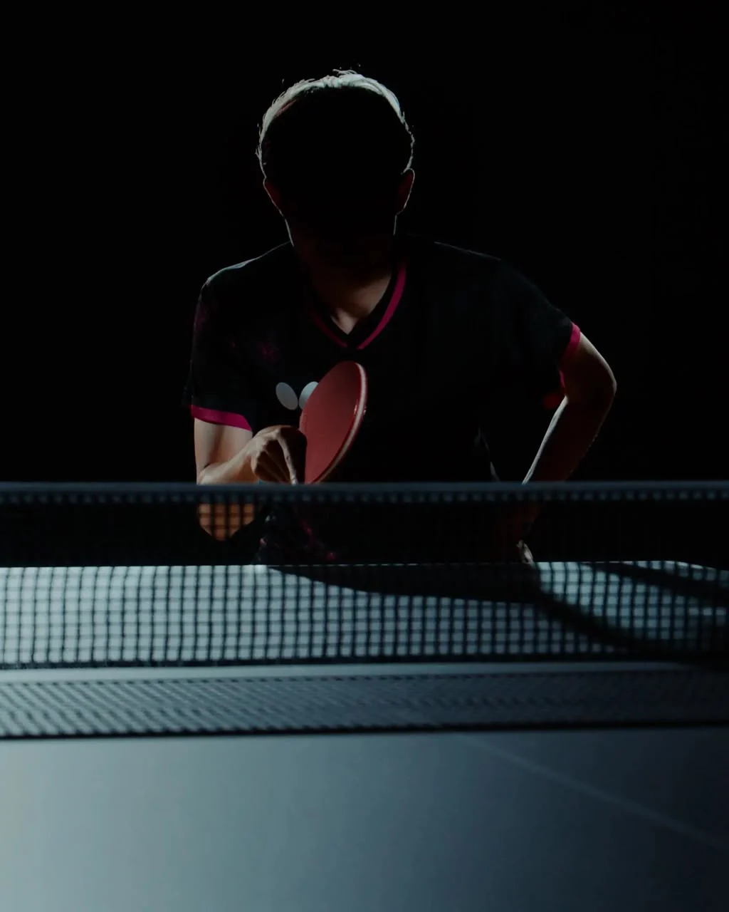 Player serving low over the net in a darkened hall